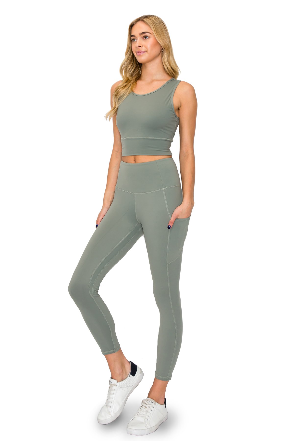 Model presenting a sage green workout set with high-waisted leggings and a complementary crop tank top.