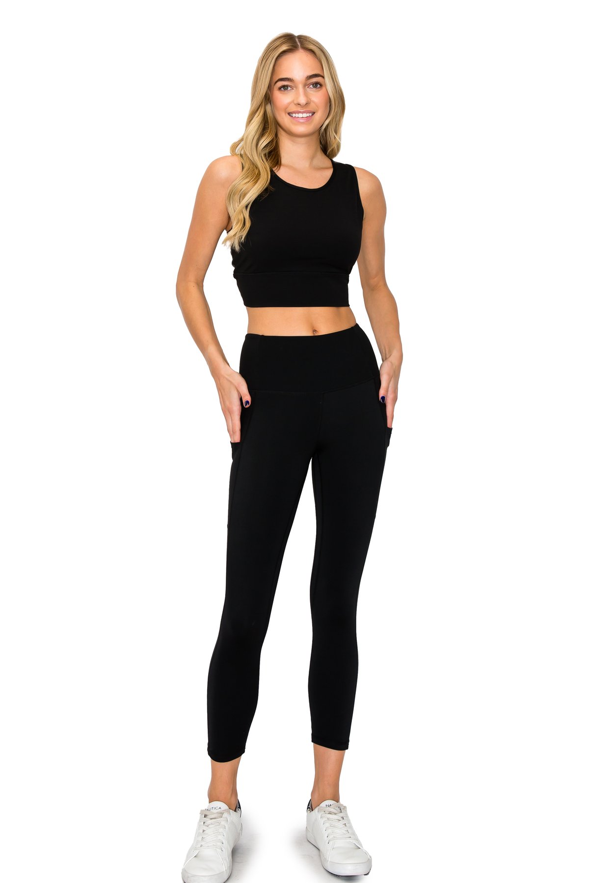 Blonde model displaying a classic black high-waisted leggings and matching crop top activewear set on a white background.