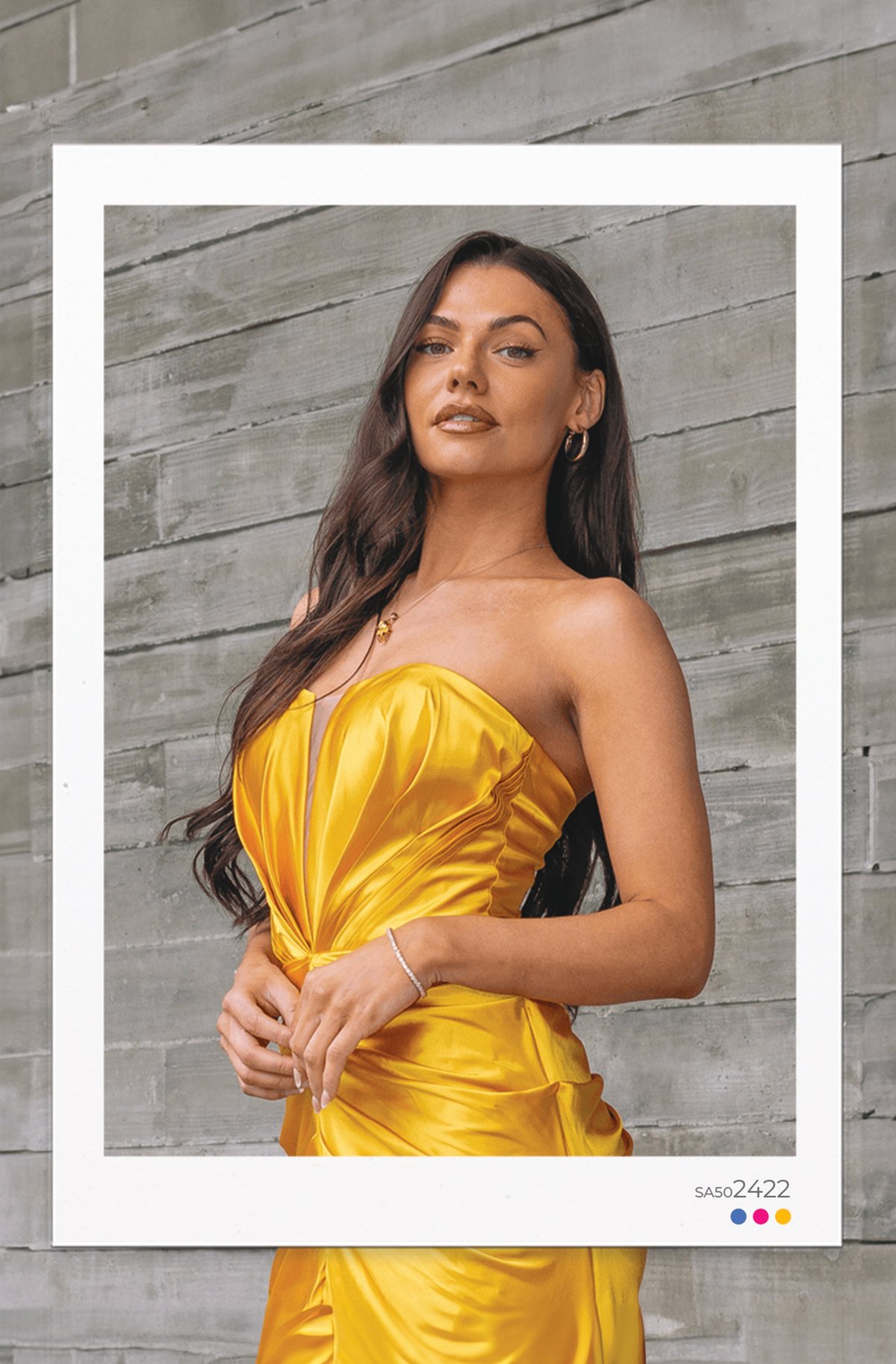 Close-up portrait of brunette model wearing a yellow strapless satin evening gown with structured bust pleating against concrete backdrop.